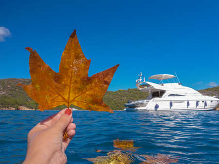 Young woman holding a maple leaf in her hand on the yacht background in the sea in autumn, Greece-October, 2020.の写真素材
