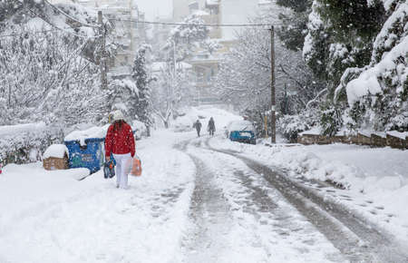 A woman goes home loaded with bags from the supermarket along a snowy street in Athens, Greece, 16th of February 2021.のeditorial素材