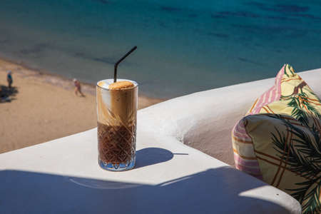Glass of yummy iced coffee or greek freddo cappuccino on the seascape background on a summer sunny day at the Kythnos, Cyclades Islands, Greece.の写真素材