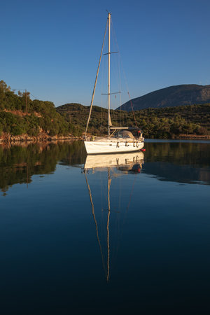 A sailing yacht at anchor in a quiet harbor on the coast of the Aegean Sea.の写真素材