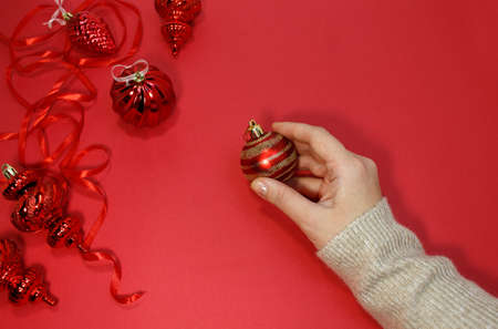 Red Christmas balls on a red background top view. A female hand holds a festive New Years decor, flat lay.の写真素材
