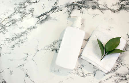 Bottle, tube, jar of shampoo, cream or lotion with white towel on a white marble. Top view. Brand...