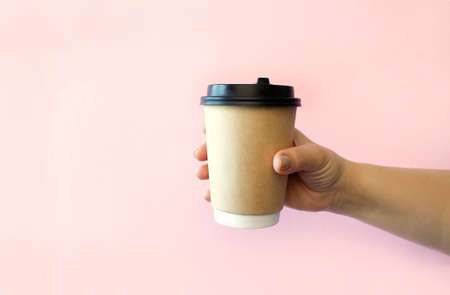 Take away coffee cup background. Female hand holding a coffee paper cup on pink background with clipping path. Close-up image.の写真素材