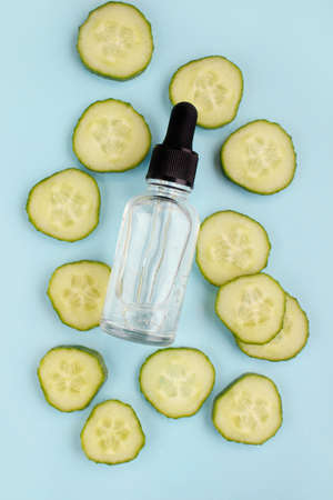 Facial lotion. Hydrating skincare gel in bottle with foam, green cucumber, blue background. Organic cosmetic treatment.の写真素材