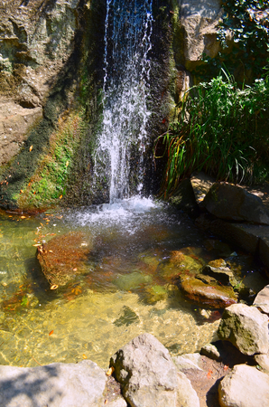 Small waterfall. Water flows on a block of stone and forms a small lake. The water that flows down from the mountains is very clean and clear, even see the sandy bottom in the form lakesの写真素材