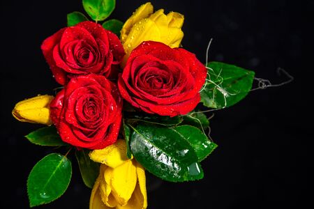 On a black background a beautiful bouquet of red roses and yellow tulipsの写真素材