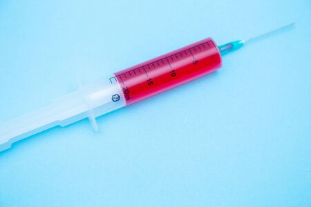 on a blue background lies a large syringe with a red medicine inside. concept. quarantineの写真素材
