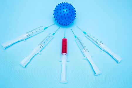 On a blue background lies a ball in the form of a coronavirus infection, around which there are large syringes with drugs for injection. Epidemic. Pandemic.の写真素材