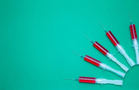 On a green background are syringes with red medicine. Concept of stopping the coronavirus. Protect...