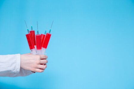 On a blue background in the hands of a girl who is dressed in a white Bicycle, a lot of large medical syringes with red injectable medicine. concept. virus.の写真素材