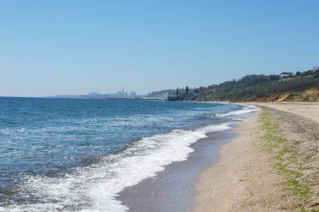 Scenic coastline with gentle waves and distant cityscape under clear blue sky. Odesa, Ukraine.の写真素材