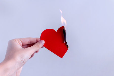 A paper red heart is burning in the hand of a woman on a violet background. Concept of unhappy love, separation, suffering.の写真素材