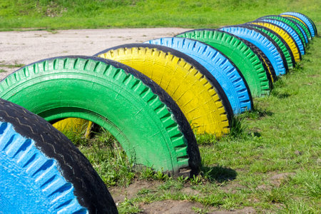 Colorful rubber tires on the green grass. Children's sports ground. Used rubber wheel for playground in park. Reuse wheel.の写真素材