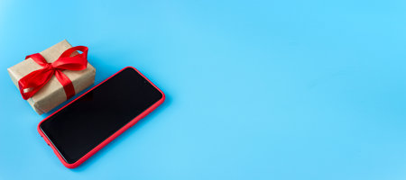 Gift box with red tape with a smartphone on a blue background. Holidays and sales concept. copyspace. Banner.の写真素材