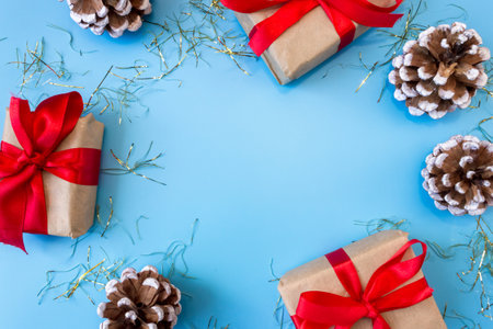 The frame of Christmas decorations gift boxes with red bows, pine cones on a blue background. postcard. copyspace. flat lay. top view.の写真素材