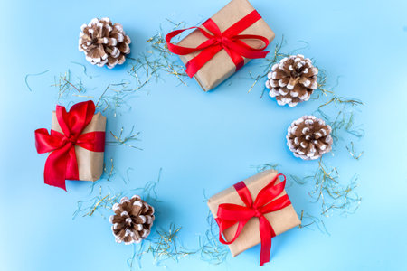 The frame of Christmas decorations gift boxes with red bows, pine cones on a blue background. postcard. copyspace. flat lay. top view.の写真素材