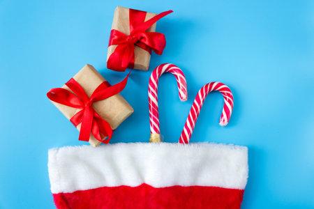 Santa Claus hat with caramel staffs and gift boxes on a blue background. postcard. The concept of Christmas and New Year.の写真素材