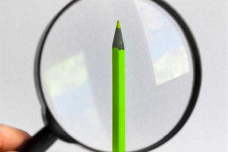 Green pencil under a magnifying glass. Minimalism concept.の写真素材