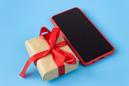 Gift box with red tape with a smartphone on a blue background. Holidays and sales concept.の写真素材