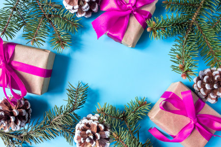 The frame of Christmas decorations gift boxes with pink bows, pine cones and spruce branches on a blue background. postcard. copyspace. flat lay. top view.の写真素材