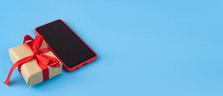 Gift box with red tape with a smartphone on a blue background. Holidays and sales concept. copyspace. Banner.の写真素材