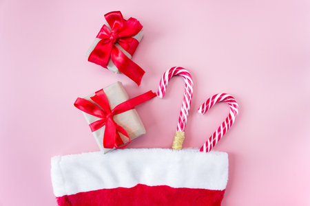 Santa Claus hat with gift box and caramel staff on a pink background. flat lay. top view. postcard. Christmas and New Year concept.の写真素材