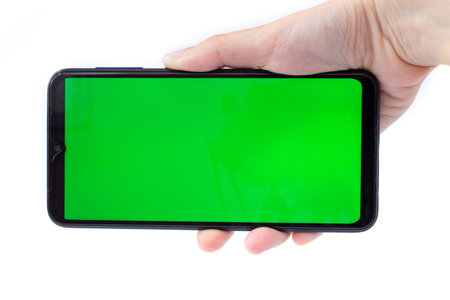 The woman's hand holds the smartphone in a horizontal position with a green screen. Chrome key. Mock up.の写真素材