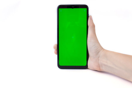 The woman's hand holds the smartphone in a vertical position with a green screen on a white background. Chrome key. Mock up.の写真素材