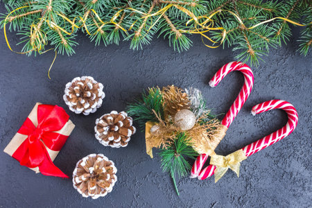 Festive gift box with spruce branches, caramel staves and pinecone on concrete background. The...
