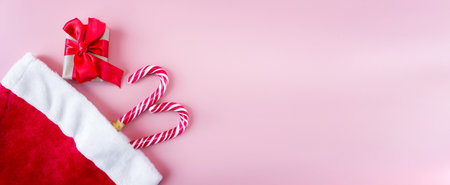 Santa Claus hat with gift box and caramel staff on a pink background. flat lay. top view. postcard. Banner. Christmas and New Year concept.の写真素材