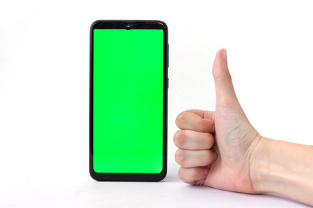 A smartphone in a vertical position with a green screen on a white background and a hand with a thumb up. Chrome key. Mock up.の写真素材