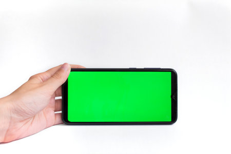The woman's hand holds the smartphone in a horizontal position with a green screen on a white background. Chrome key. Mock up.の写真素材