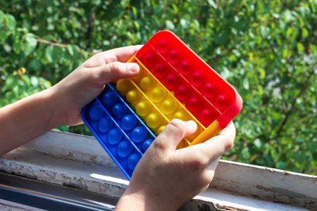 Children's hands holds an antistress toy popit on the window.の写真素材
