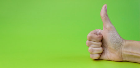 Hand with thumbs up on a green background close up. copyspace. Banner.
