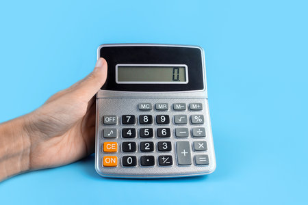 Hand with a calculator on a blue background. The concept of finance, business, money, accounting, savings.の写真素材