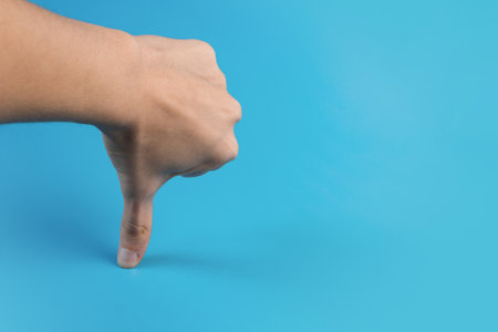 Female hand with thumb down on blue background. copyspace.の写真素材