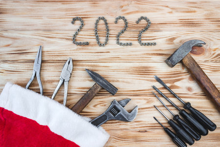 Carpentry tools in Santa Claus hat on a light wood table with 2022 lined with screw nuts. The concept of New Year and Christmas in the construction industry. top view. flat lay.の写真素材