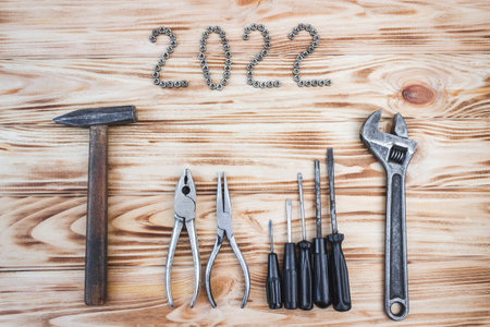 Carpentry tools on a light wood table with 2022 lined with screw nuts. The concept of New Year and...