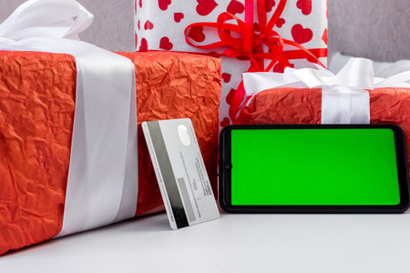 Smartphone with green horizontal screen and credit card on white table with beautiful Christmas boxes. mockup for application presentation. Chrome key. Online payments concept.の写真素材