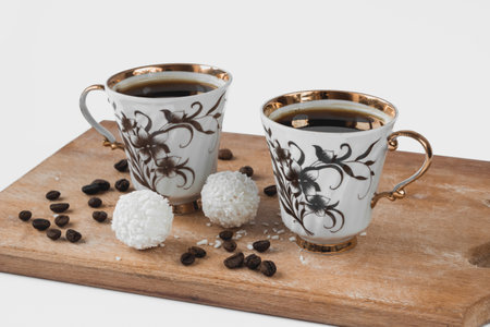 Two white cups of coffee on a wood board with grains and candy made of coconut shavings.の写真素材