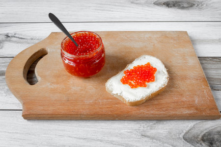 Red salmon caviar in a jar and on a butter sandwich.の写真素材
