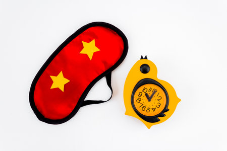 Red sleep mask with yellow alarm clock on a white background. Insomnia, rest and healthy sleep concept. top view.の写真素材