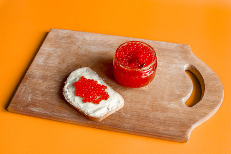 Red salmon caviar in a jar and on a butter sandwich. orange background.の写真素材