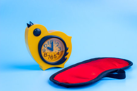 Red sleeping eye mask, yellow alarm clock on a blue background. Insomnia, rest and healthy sleep concept.の写真素材