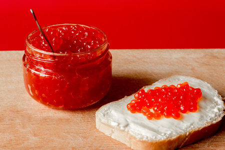 Red salmon caviar in a jar and on a butter sandwich. red background.の写真素材