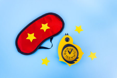 Red sleep mask with yellow alarm clock on a blue background. Insomnia, rest and healthy sleep concept. flat lay.の写真素材