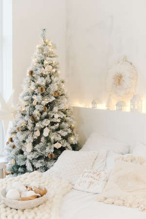 Light cozy bedroom decorated for celebrating Christmas. Eco style interior in white colors with tender pind linen on a bed. Xmas in a bed room. Christmas concept. Bedroom in christmas interior.の写真素材