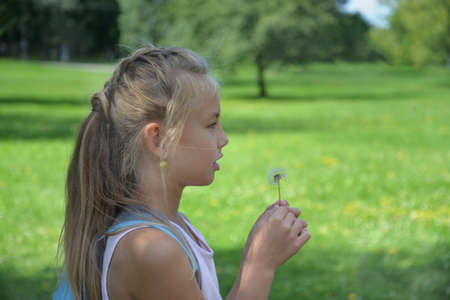 Eight-year-old girl on a green background of a Park holding a dandelion and making a wish, Russia.の写真素材