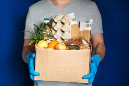 Male courier, protective gloves with a grocery box with fresh food home delivery during the coronavirus quarantine, close-up.の写真素材