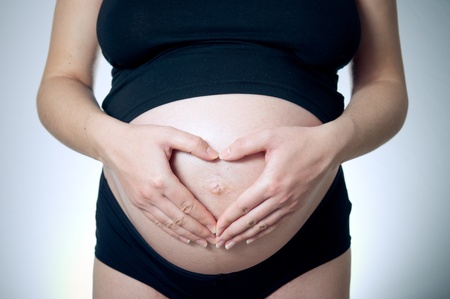 Woman holding her hands in a heart shape on her pregnant belly